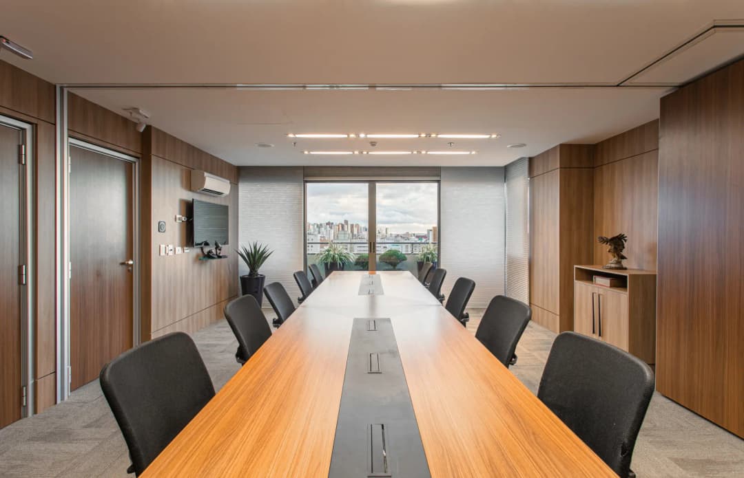 Sala de reuniões sofisticada com ar-condicionado, mesa de madeira, com 12 lugares e paredes forradas com painéis de madeira, localizado em Curitiba - Paraná.