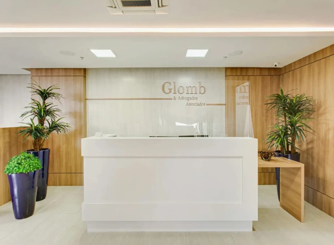 Entrada do escritório de advocacia Glomb Advogados, maior especialista em direito do trabalho e direito previdenciário do Brasil. Balcão da recepção branco com uma parede de mármore atrás e a logo do escritório.