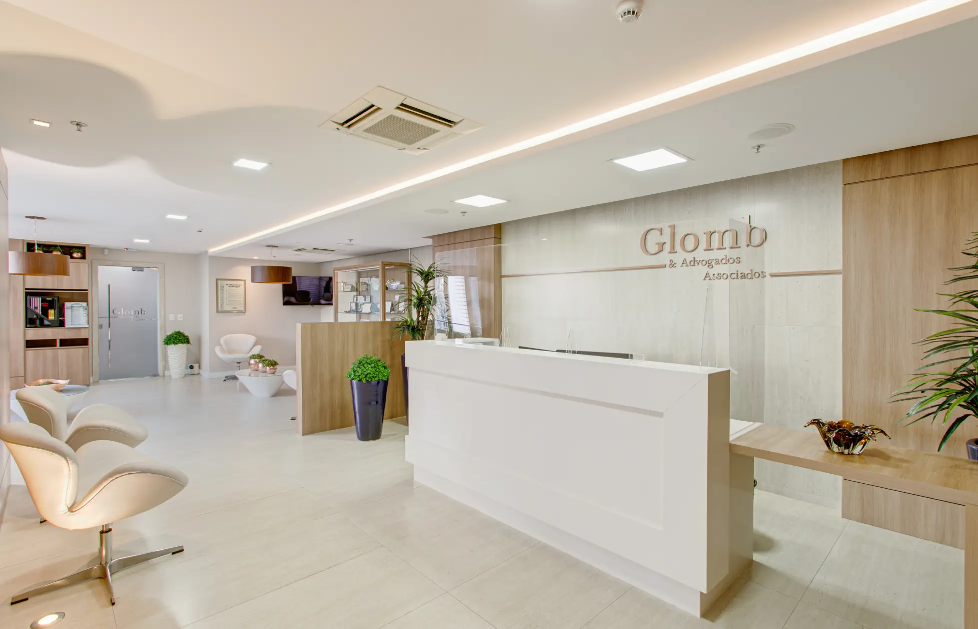 Recepção do escritório de advocacia Glomb & Advogados Associados, especializado em direito do trabalho e previdenciário. Piso em mármore claro, com cadeiras brancas modernas e paredes com painéis de madeira.